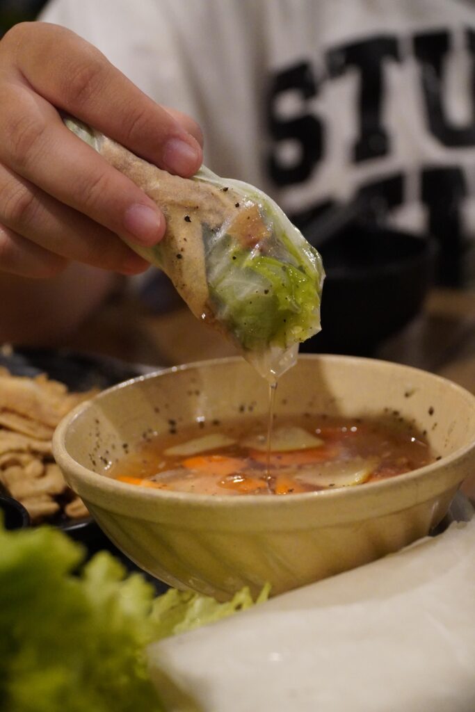Vietnamese nem thinh rice paper roll being dipped into a flavorful traditional sauce