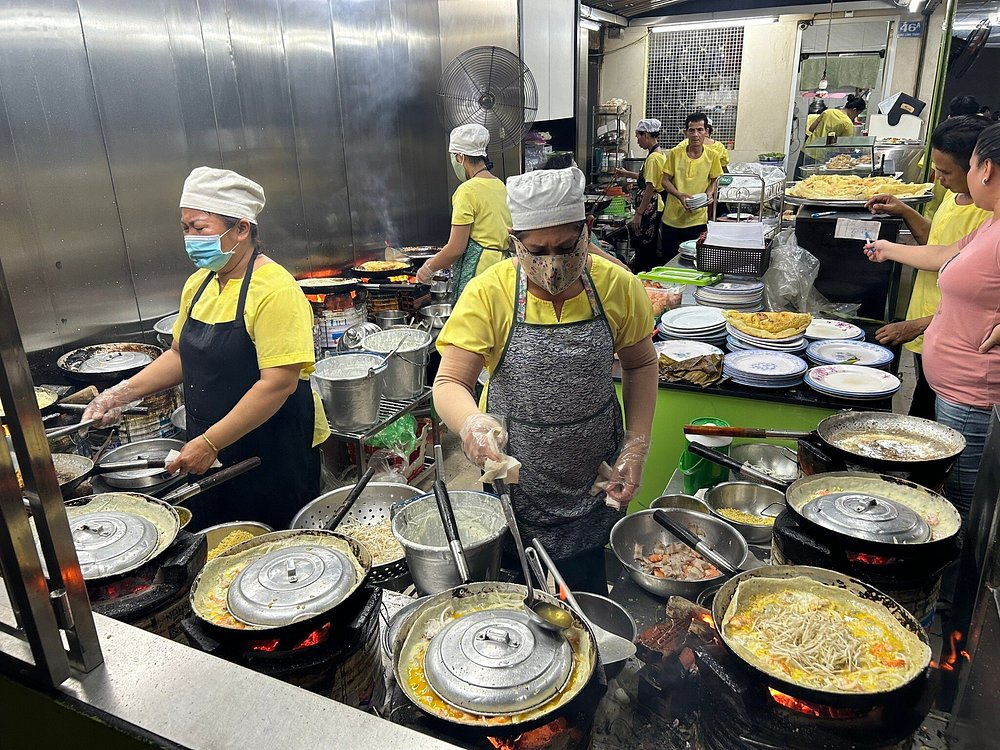 A busy kitchen with multiple chefs preparing sizzling bánh xèo on open flames