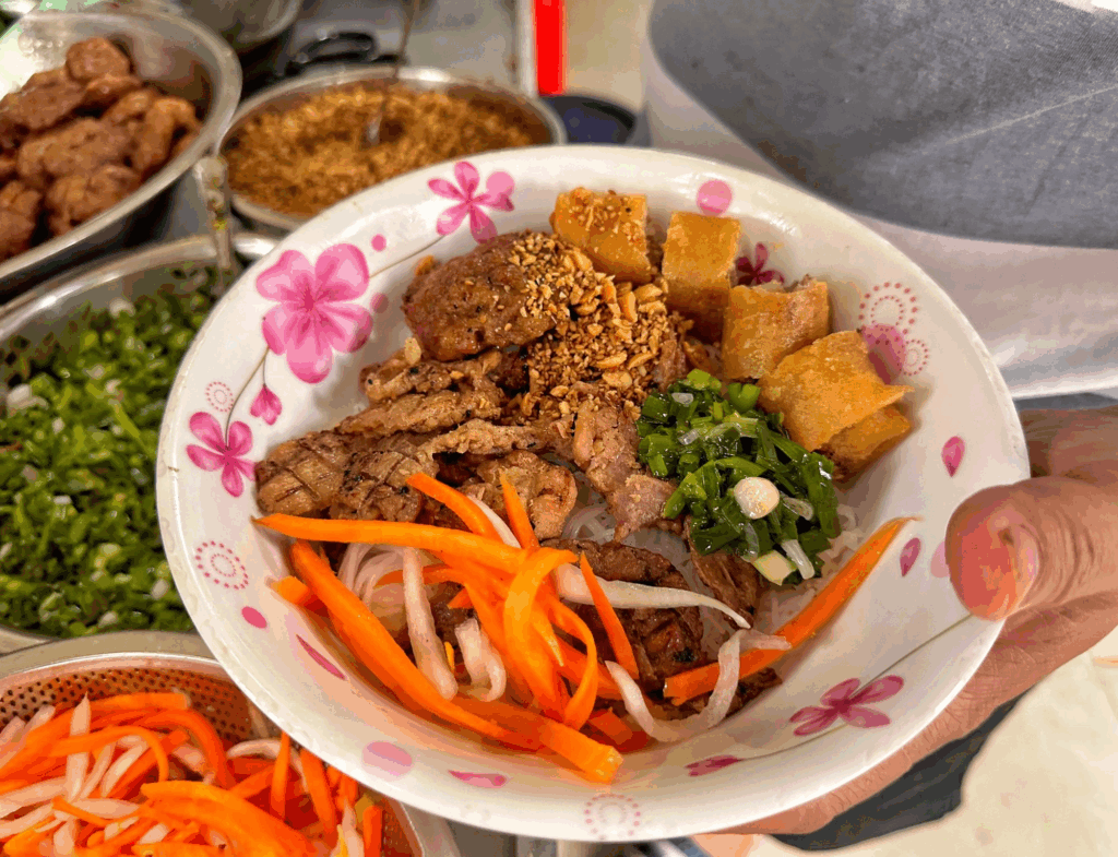 Colorful bowl of grilled pork noodles with pickled vegetables and crispy toppings in Ho Chi Minh City