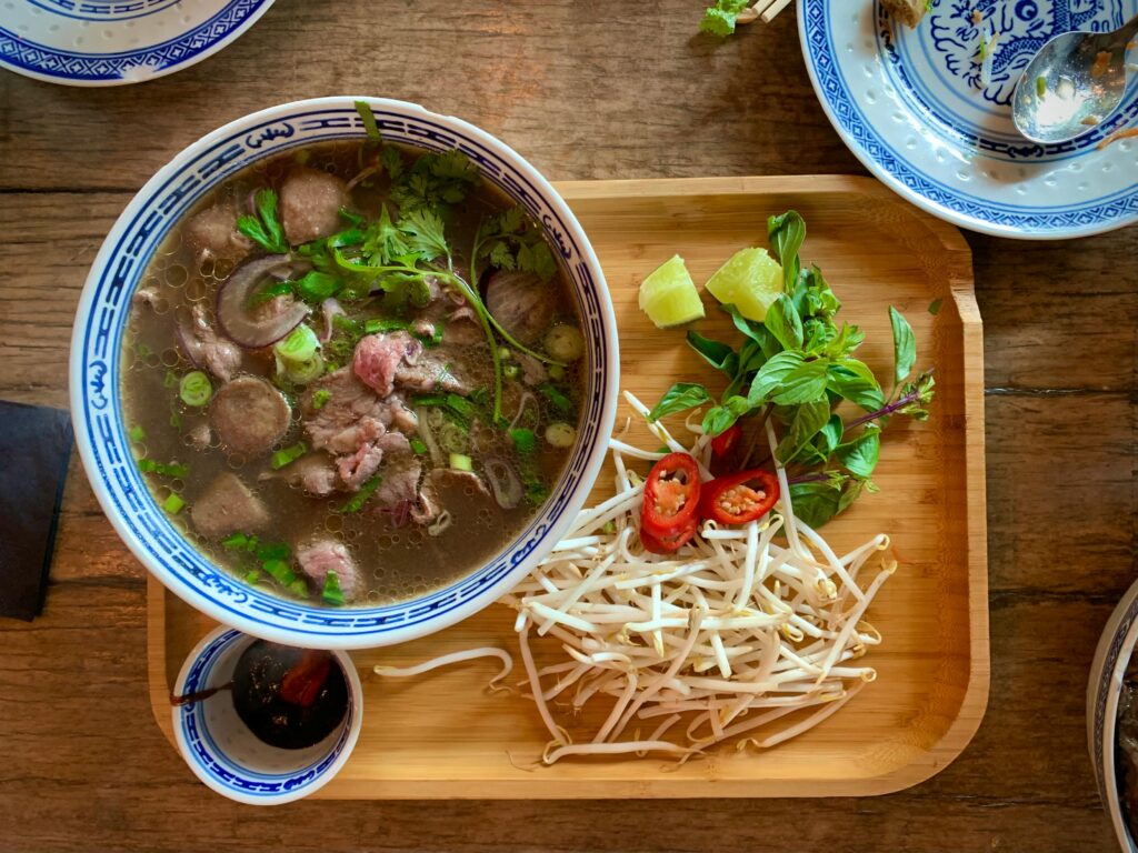Traditional Vietnamese pho served with herbs, bean sprouts, lime, and chili on a wooden tray