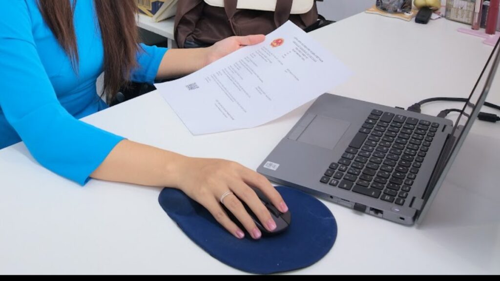 KissTour staff holding a signed Vietnam visa approval document beside a laptop while processing a Vietnam visa in 1 hour request