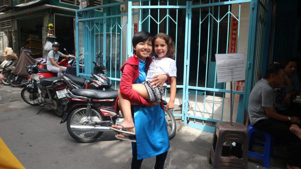 KissTour guide holding a young girl next to parked motorbikes on a Saigon motorbike tour with kids