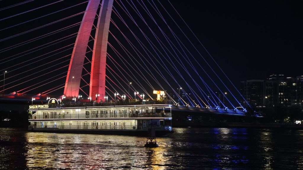 Saigon dinner cruise boat passing under the red-lit Ba Son Bridge at night