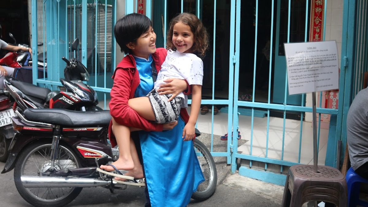 Tour guide carrying a smiling child beside parked motorbikes before a Saigon motorbike tour with kids