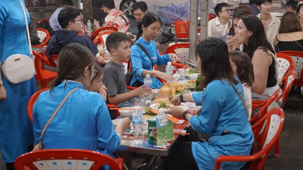 A busy street-side table in Saigon with guests, guides and shared dishes