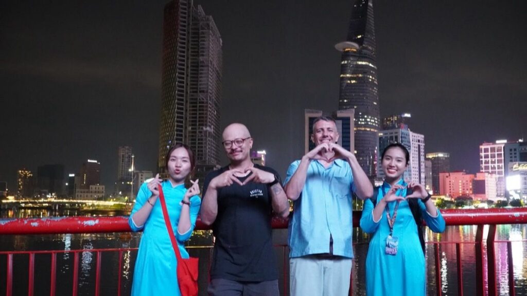 Guests on Bach Dang riverfront with Saigon skyline lit at night
