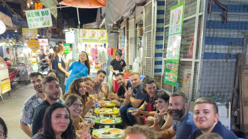 Guests and KissTour guides sharing dishes at a street-side table on a Saigon food tour