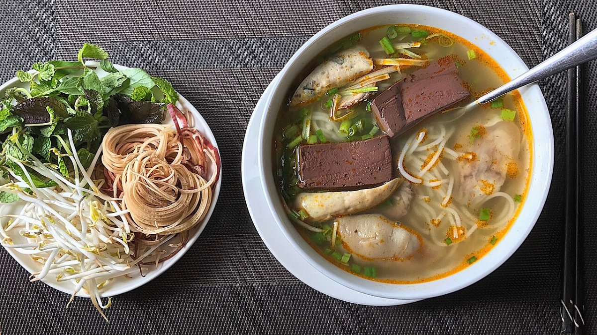 A bowl of bun bo hue with noodles, beef and herbs
