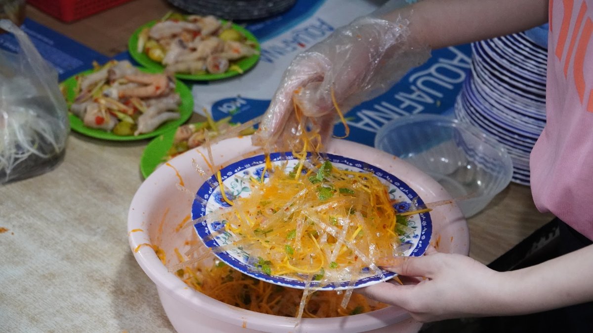 A bowl of turmeric-yellow Mi Quang noodles being served at a Da Nang street-food stall